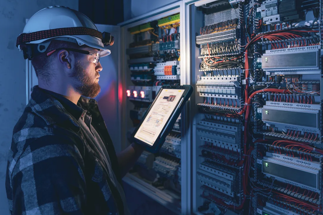 A worker with a tablet inspecting an electrical control panel